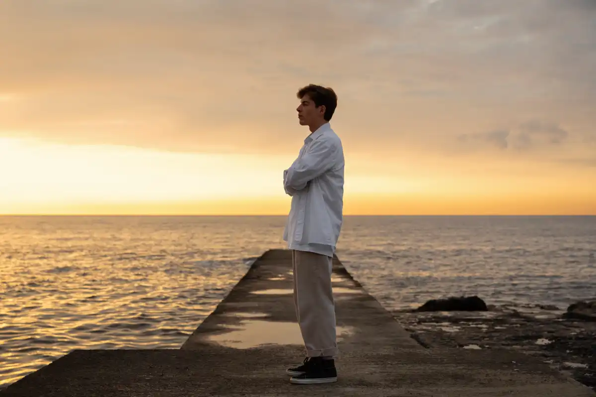 Man standing alone on a seaside pier at sunset, looking toward the horizon in a moment of quiet reflection, symbolising loneliness, emotional isolation, and self-contemplation.