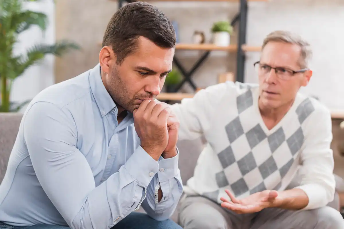 Young man discussing health concerns with an older man, with both sitting outdoors during a supportive conversation.