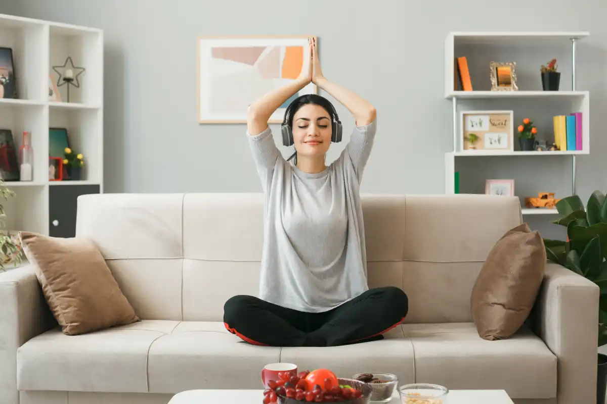 Woman practicing yoga meditation at home on a sofa, promoting relaxation, mindfulness, and healthy living.