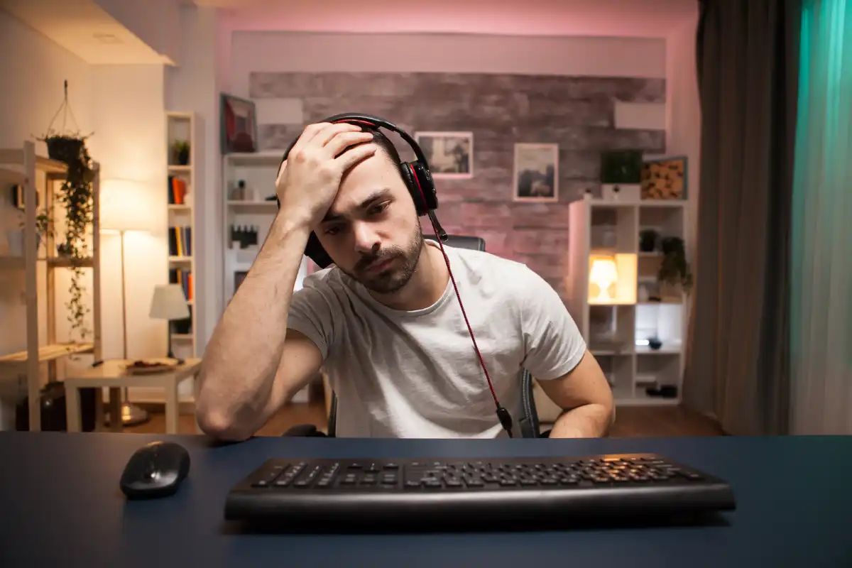 Stressed man sitting at a desk with his head in his hands while working on a computer.