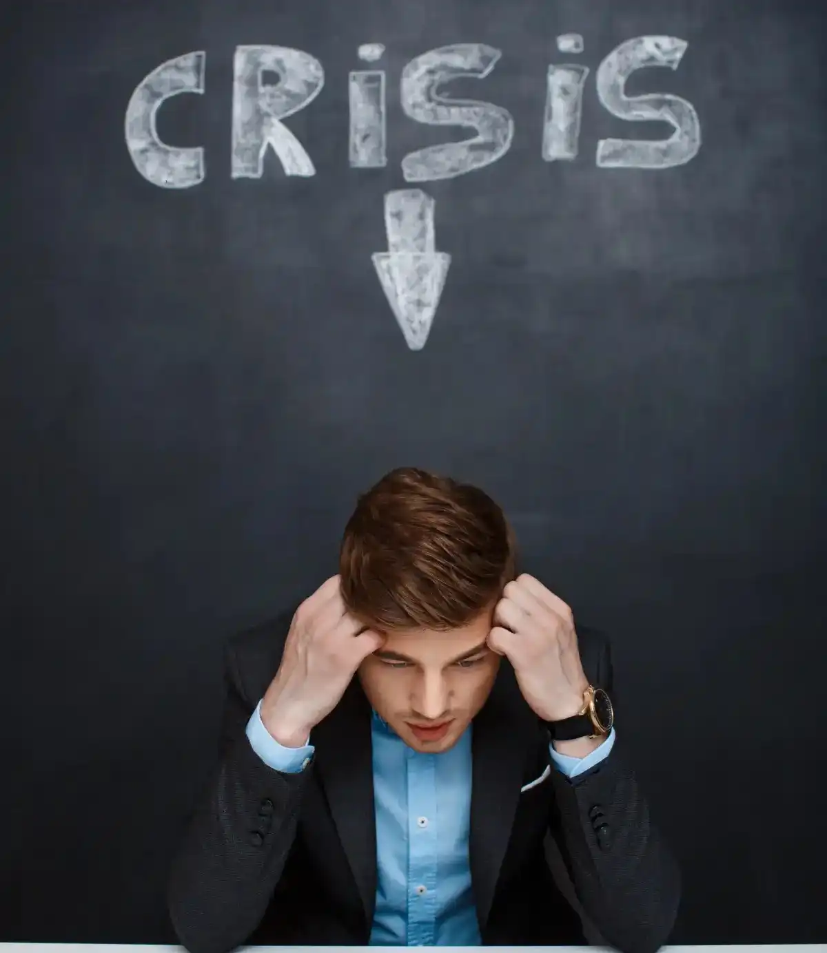 A stressed office professional sitting with their head in their hands beneath the word “CRISIS,” representing workplace stress, pressure, or an emotional crisis.